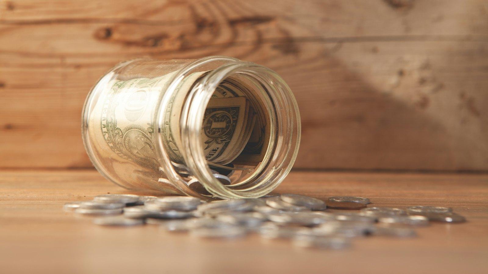 Coins spilling from a glass jar onto a wooden table