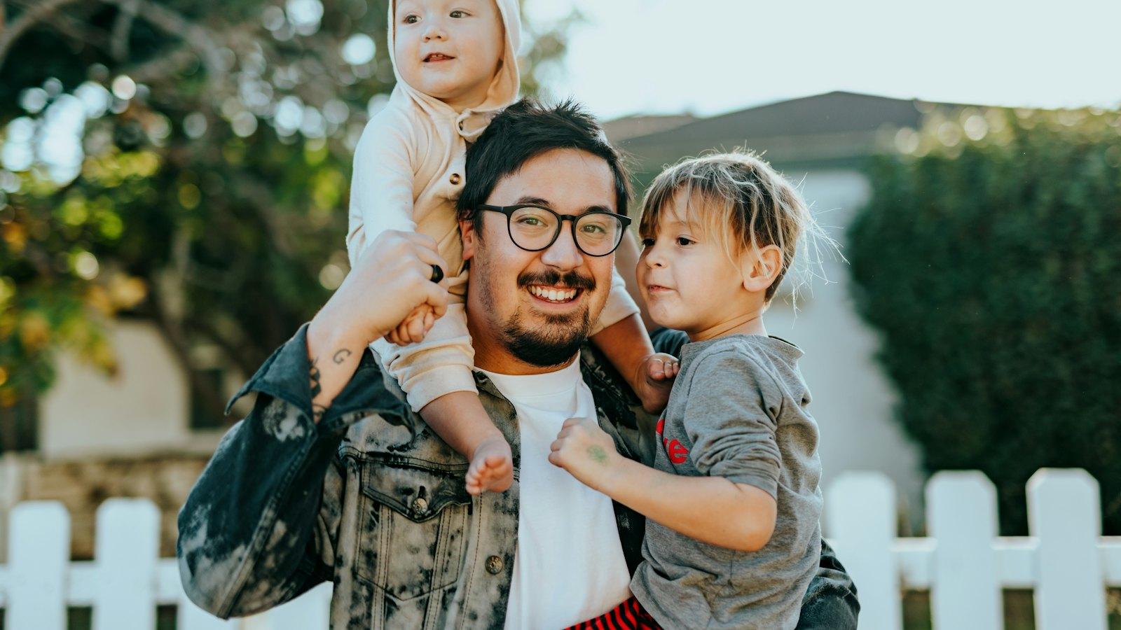 Father carrying his two young children on his shoulders outside their home