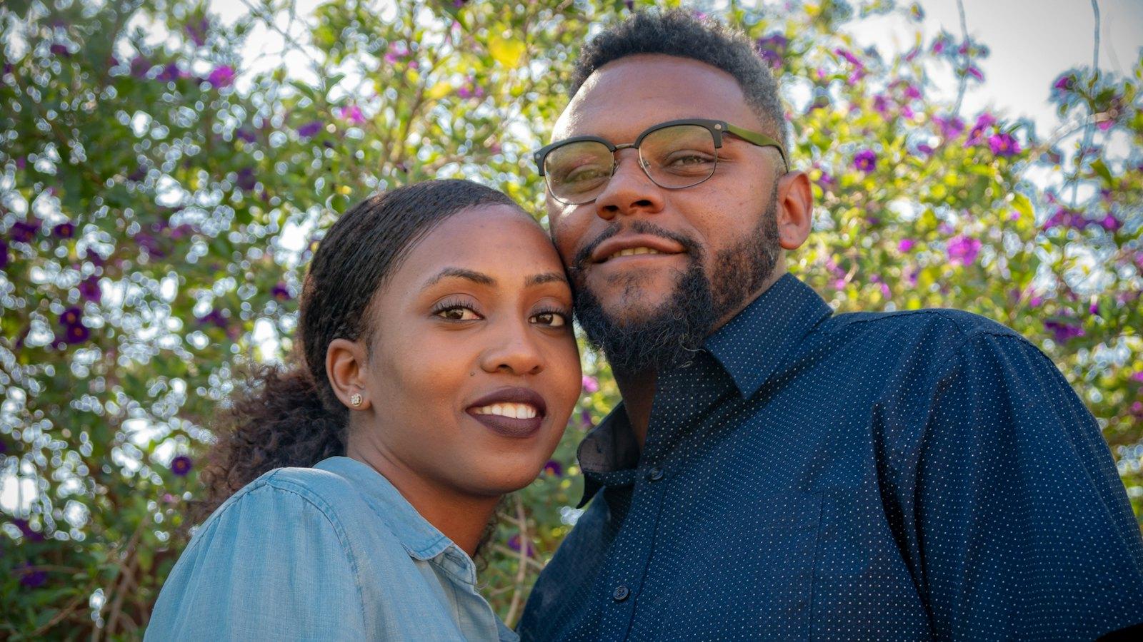 Young couple smiling outdoors in front of flowering bushes