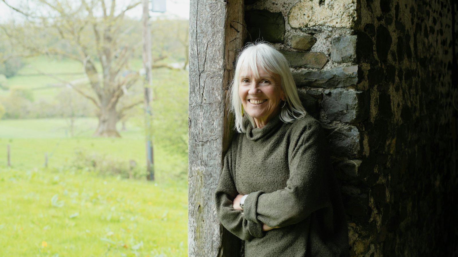 Smiling woman in her eighties leaning against a stone wall