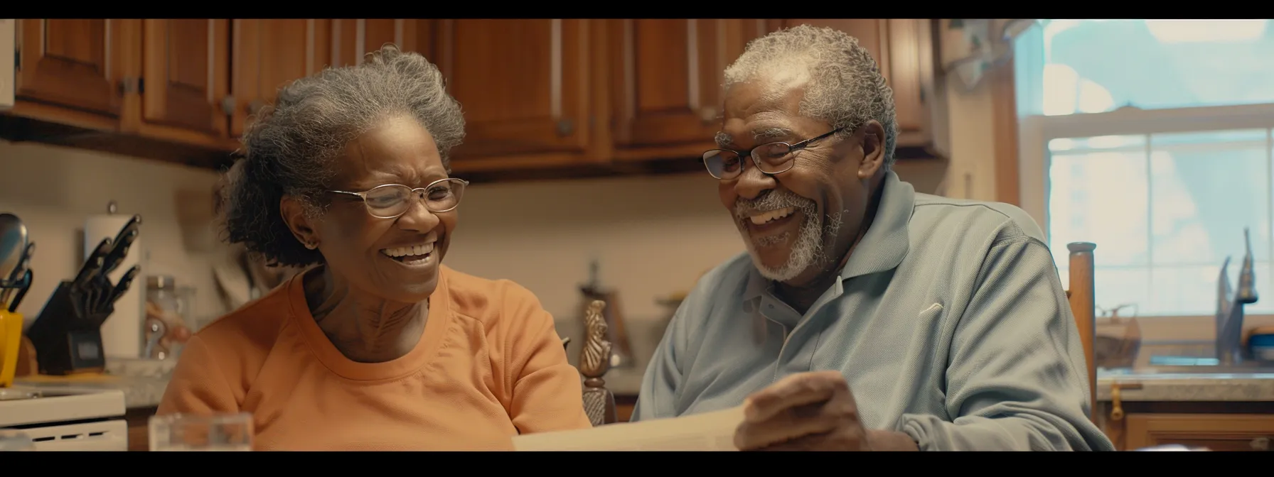 a senior couple smiling happily while reviewing medicare enrollment materials at their kitchen table.